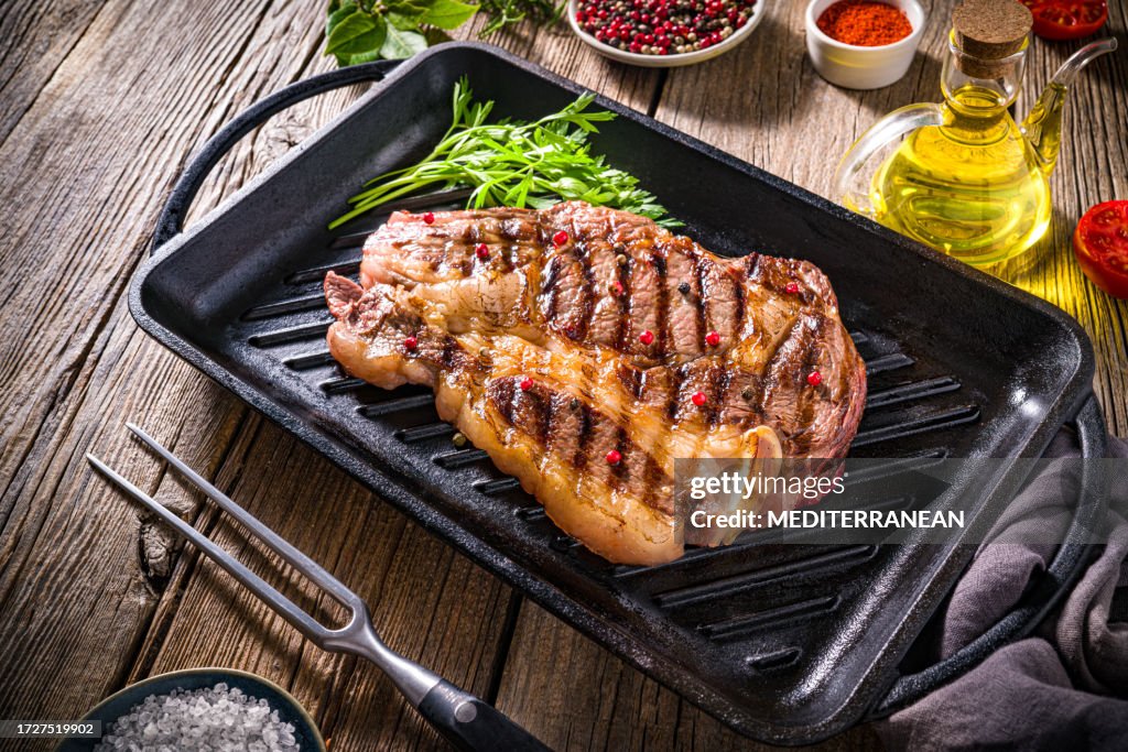 Beef rib steak grilled on cast iron grill with herbs olive oil, tomato, pepper ingredients