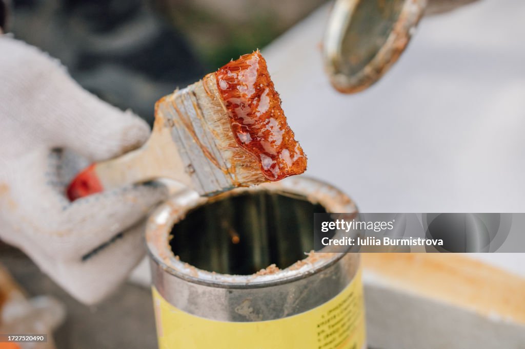 Close-up view of hand of unrecognizable person wearing gloves, holding paintbrush with remnants of red paint or varnish