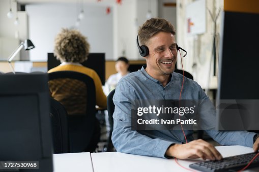 Happy male customer service representative working on PC in call center. Happy male customer service representative working on PC in call center.