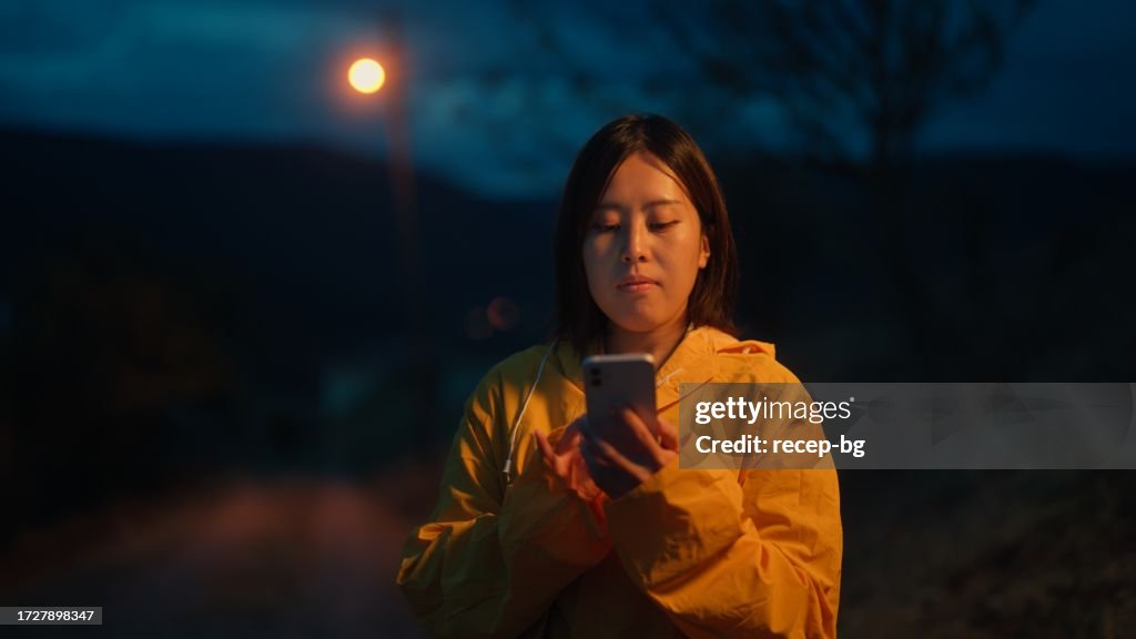 Female Asian traveler using her mobile smart phone in nature at night