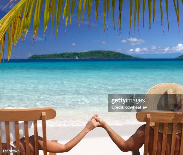 couple relaxing in teak chairs on beautiful beach - veleiding stockfoto's en -beelden