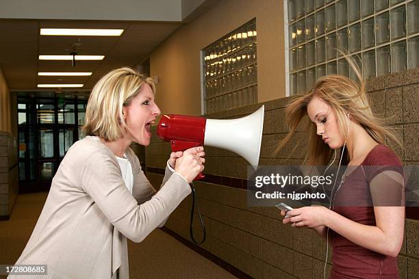 woman yelling through a bullhorn at an unfazed teenage girl - angry men stockfoto's en -beelden