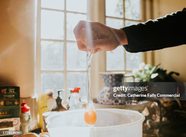 a man breaks an egg into a mixing bowl from a height, using one hand. - hand holding whisk stock pictures, royalty-free photos & images