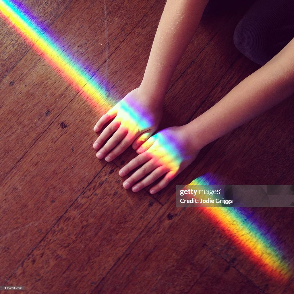 Rainbow light crossing hands of a child on ground