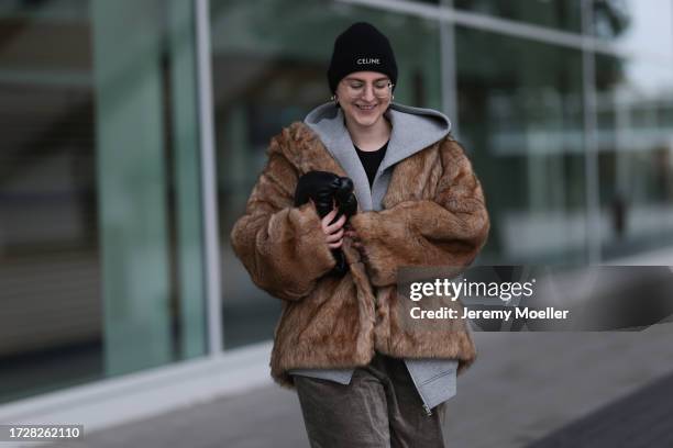 Maria Barteczko is seen wearing round retro glasses with golden frame from Ray-Ban, golden logo earrings from Chanel, a black knitted logo beanie...