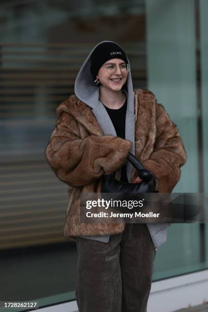 Maria Barteczko is seen wearing round retro glasses with golden frame from Ray-Ban, golden logo earrings from Chanel, a black knitted logo beanie...