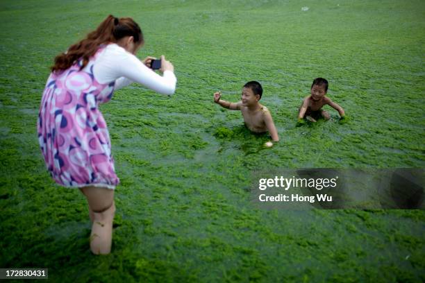 Children swim in sea water covered in a thick layer of green algae on July 05, 2013 in Qingdao, China. A large quantity of non-poisonous green...