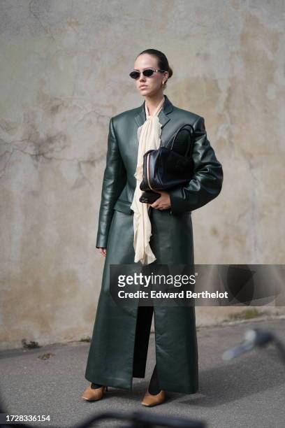 Guest wears sunglasses, a beige gathered long scarf, a green leather long jacket, a leather bag, outside Givenchy, during the Womenswear...