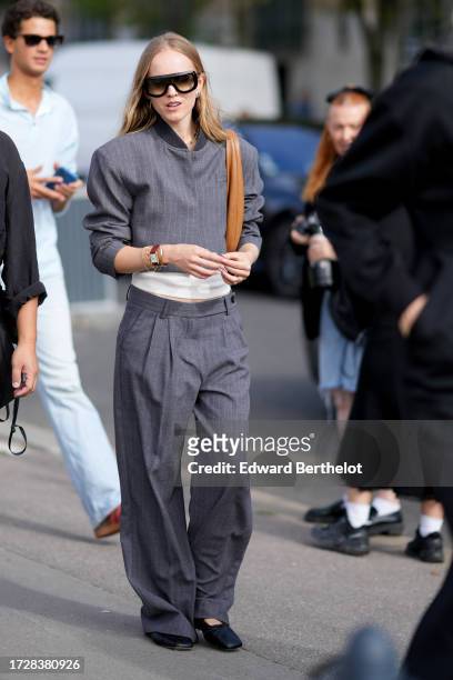 Guest wears sunglasses, a gray striped jacket, a white top, matching suit pants, outside Givenchy, during the Womenswear Spring/Summer 2024 as part...