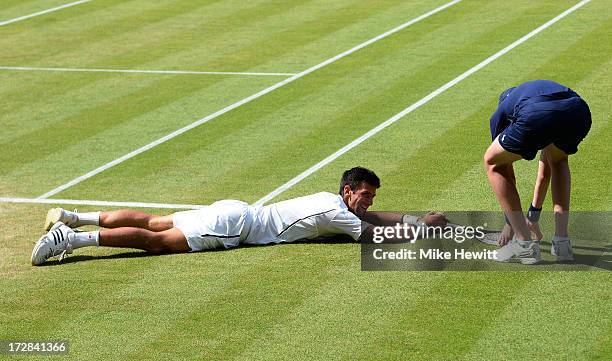 Novak Djokovic of Serbia smiles after falling on the grass as a ballboy picks up his racquet for him during the Gentlemen's Singles semi-final match...