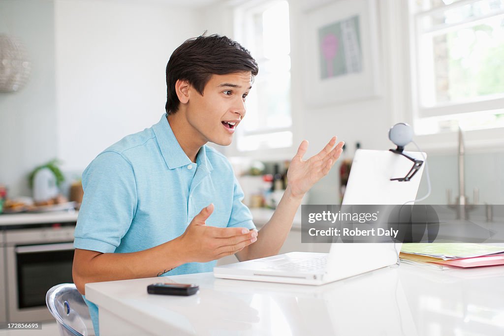 Teenage boy with cell phone having video chat on laptop