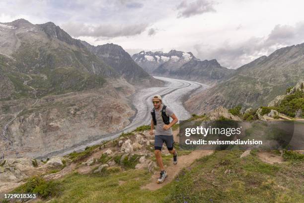 trail runner ascends alpine path in swiss mountain landscape, glacier in the background - aletsch glacier stock pictures, royalty-free photos & images