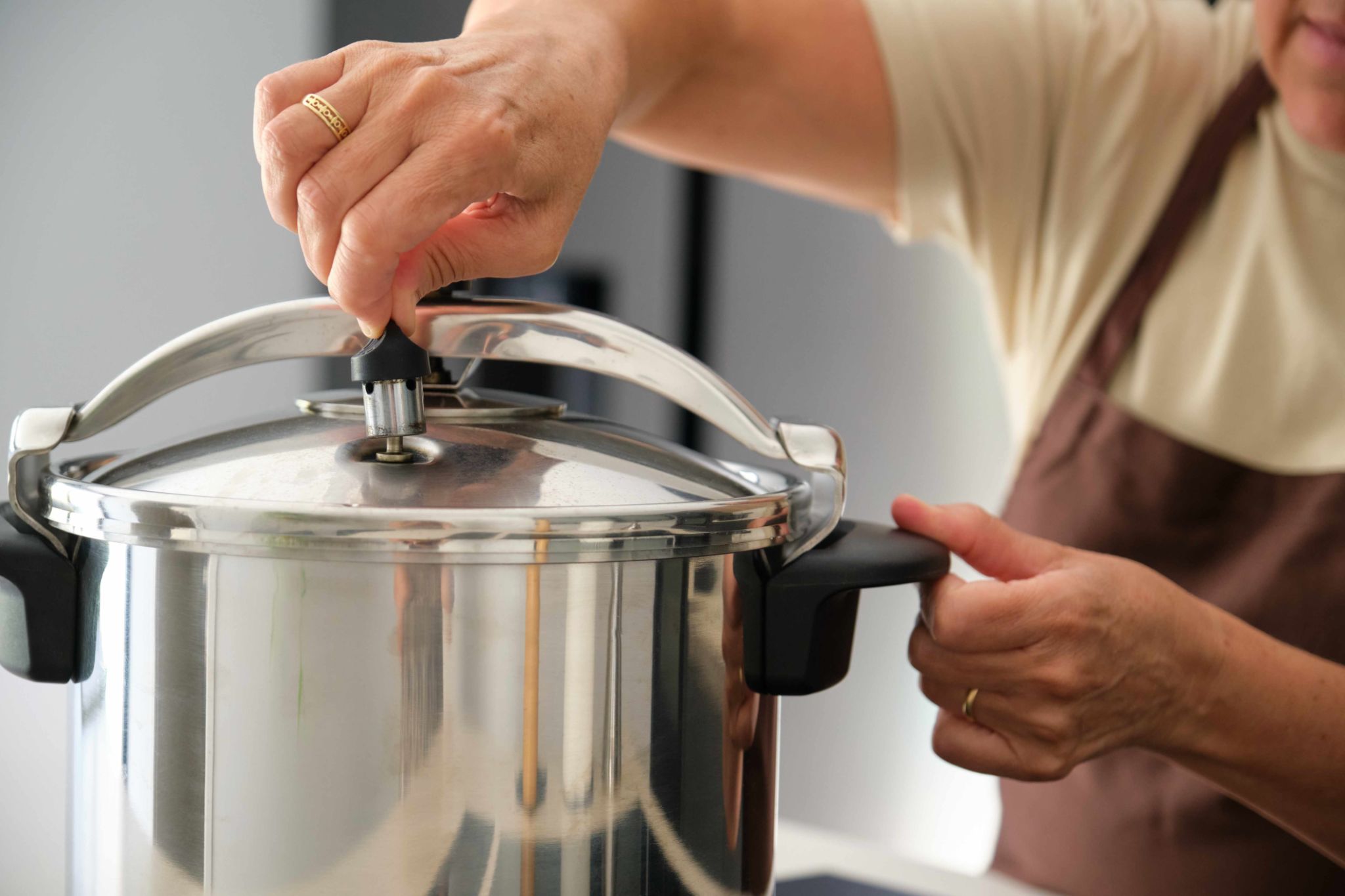 Mature Spanish woman placing regulator whistle on pressure cooker. Mature Spanish woman placing regulator whistle on pressure cooker.