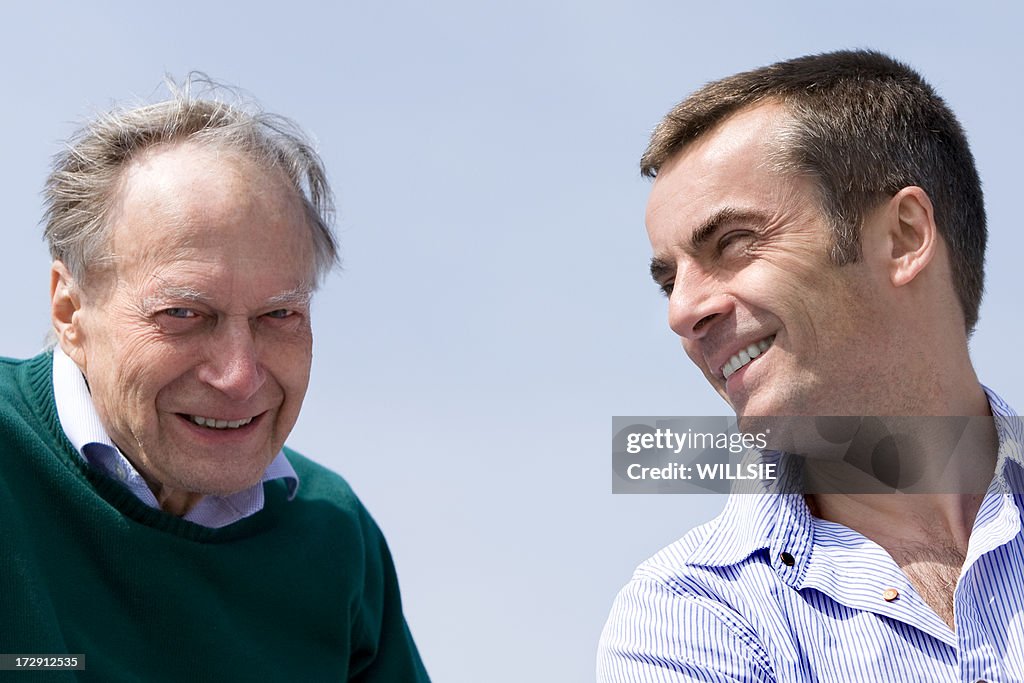 Middle aged son and senior father together against blue sky