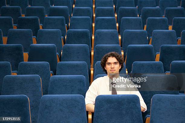 man sitting alone among empty blue seats in an auditorium - auditorium seats stock pictures, royalty-free photos & images