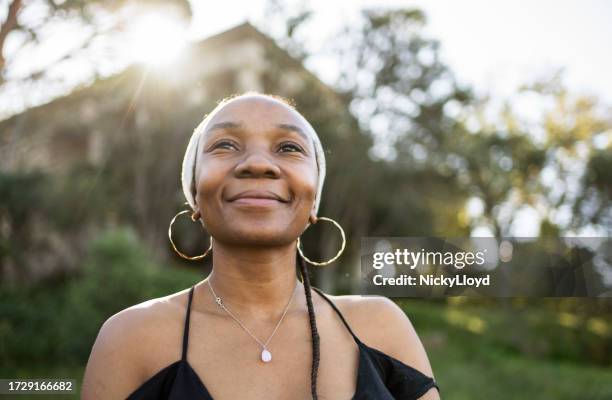 stylish young woman standing outside in the late afternoon and smiling - sleeveless dress stock pictures, royalty-free photos & images