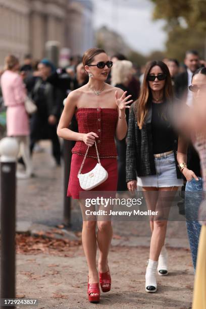 Guest is seen outside Chanel show wearing black Chanel sunnies, silver shiny Chanel earrings, necklace and bracelet, burgundy colored tweed top with...