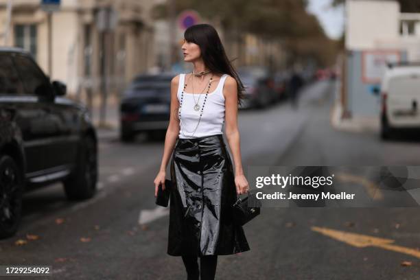 Leia Sfez is seen outside Chanel show wearing silver and black Chanel necklaces, white tank top and black wide patent skirt and black leather handbag...