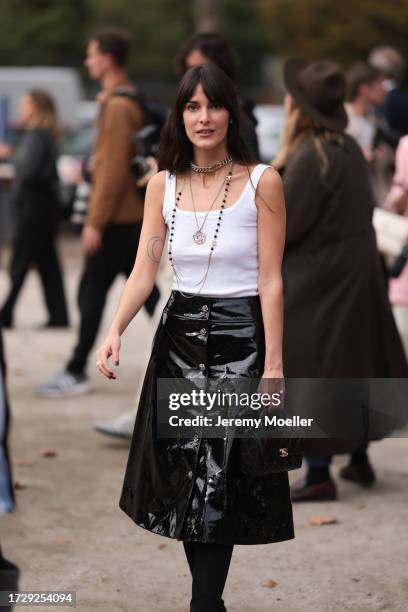 Leia Sfez is seen outside Chanel show wearing silver and black Chanel necklaces, white tank top and black wide patent skirt and black leather handbag...