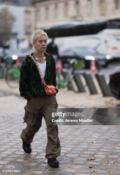 Guest is seen outside Chanel show wearing golden Chanel necklaces, leopard printed cardigan in green and red, dark green cargo pants, orange colored...