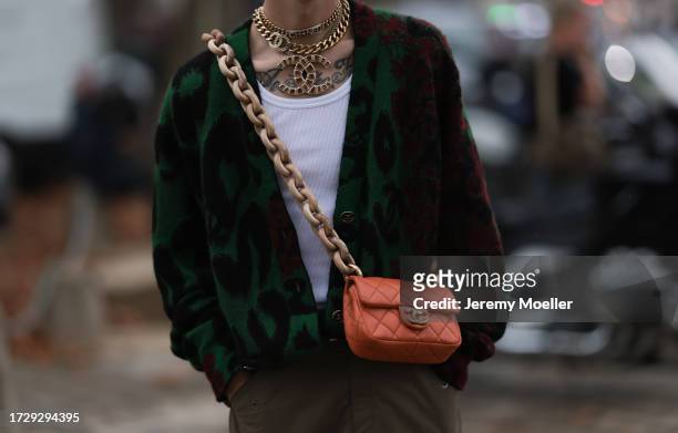 Guest is seen outside Chanel show wearing golden Chanel necklaces, leopard printed cardigan in green and red, dark green cargo pants, orange colored...