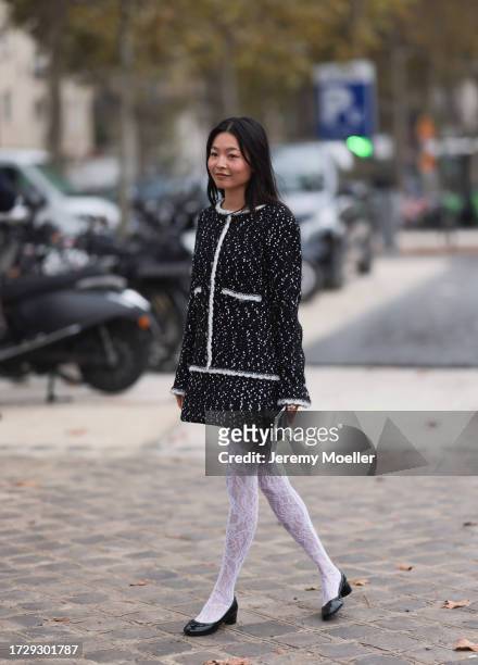 Guest is seen outside Chanel show wearing black and white tweed Chanel jacket and matching short skirt, white lace tights and black patent ballet...
