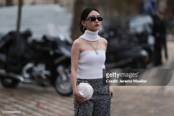 Guest is seen outside Chanel show wearing black Chanel logo sunnies, silver Chanel necklace, white knitted top wrapped around neck, black and white...