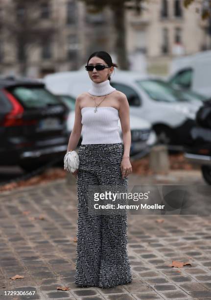Guest is seen outside Chanel show wearing black Chanel logo sunnies, silver Chanel necklace, white knitted top wrapped around neck, black and white...