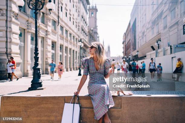 beautiful woman with sunglasses looking away while sitting on the city wall - milão imagens e fotografias de stock