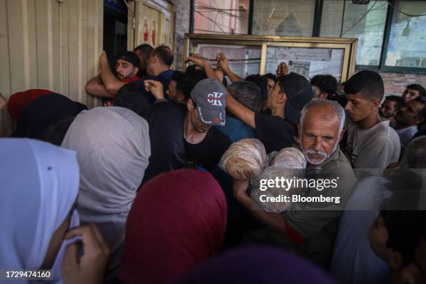 Palestinian man holds bread near a queue of people waiting to collect limited food supplies at a store in Khan Younis, Gaza, on Monday, Oct. 16,...