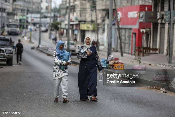 Palestinian women carry their bottles of water after Israeli authorities have ceased supplying electricity, water and food as Israeli airstrikes...