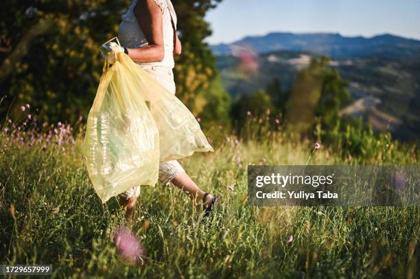 side view of a woman walking and holding trash bag in a meadow. - people picking up trash stock pictures, royalty-free photos & images