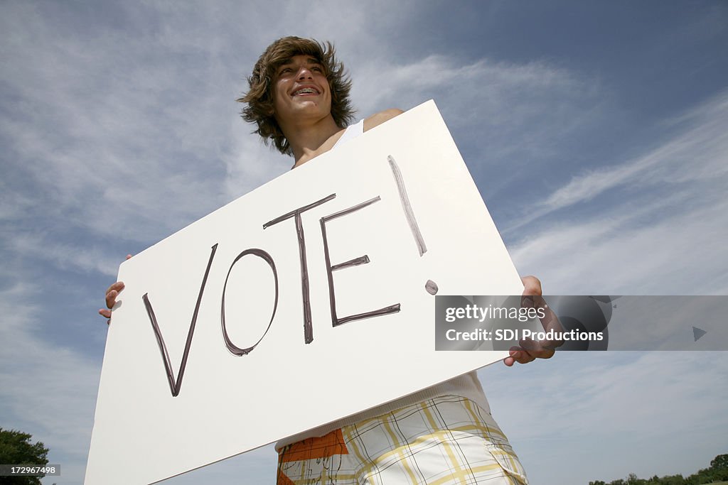 Young Male Outside Holding Large Sign That Says Vote