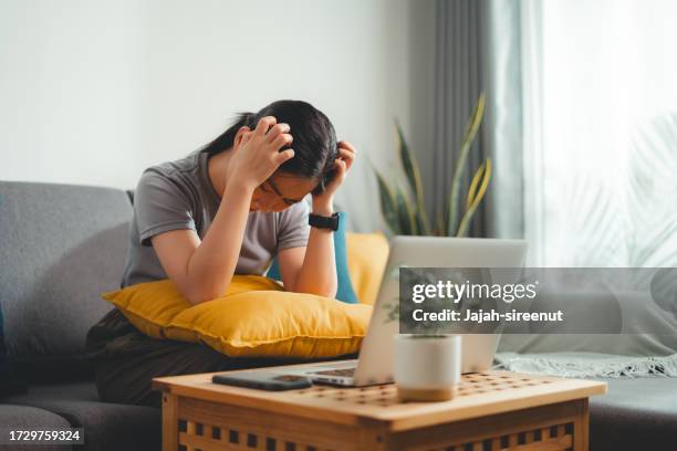 mujer asiática rascándose la cabeza, sentada en el sofá de la sala de estar de su casa. - caspa fotografías e imágenes de stock