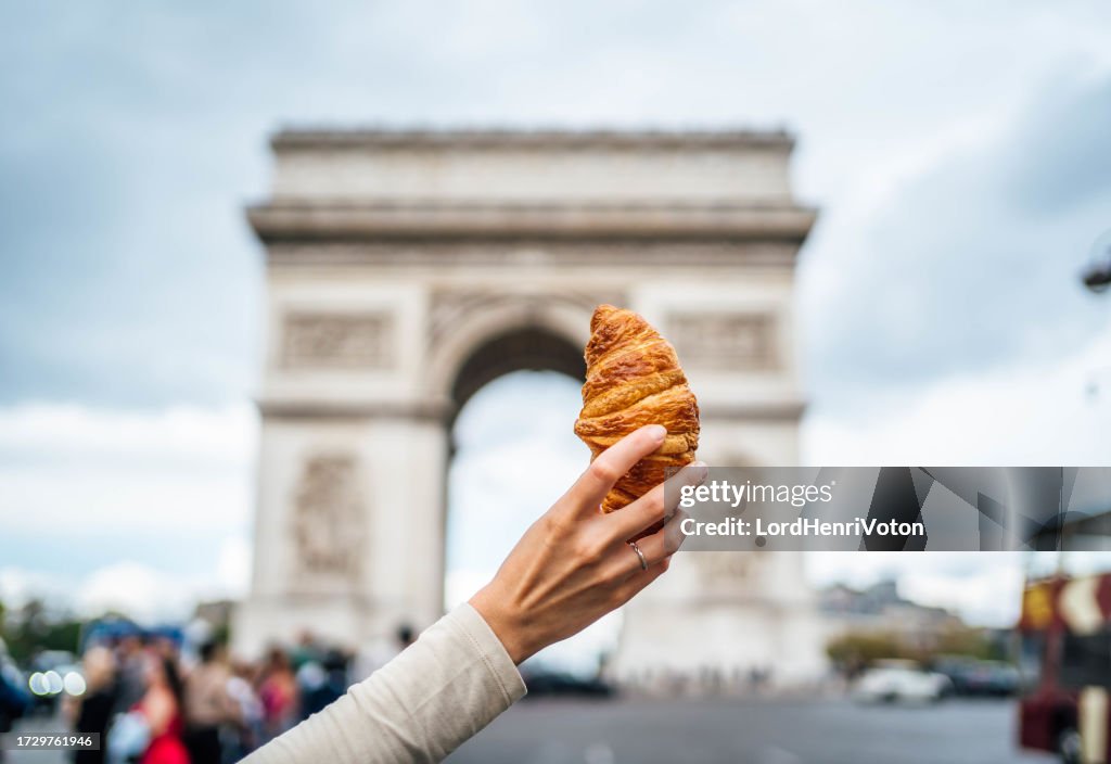 Woman holding croissant in front of the famous Arc de Triomphe