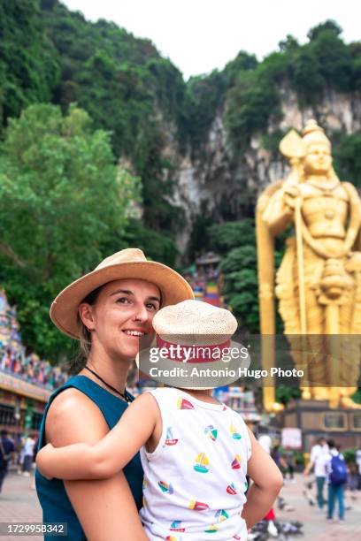 smiling woman holding her child in her arms looking at the camera. in the background batu caves in malaysia - thaipusam stock pictures, royalty-free photos & images