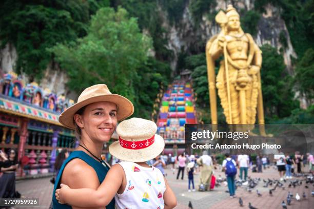 smiling woman holding her child in her arms looking at the camera. in the background batu caves in malaysia - thaipusam stock pictures, royalty-free photos & images