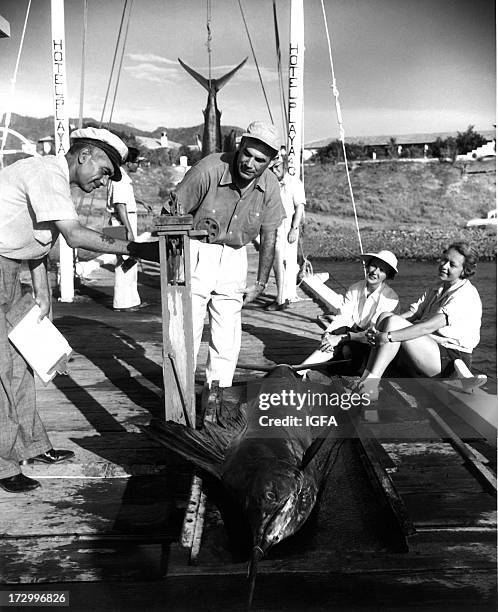 Two women look on as two men weigh a sailfish at the Hotel Playa dock in Mexico circa 1950.