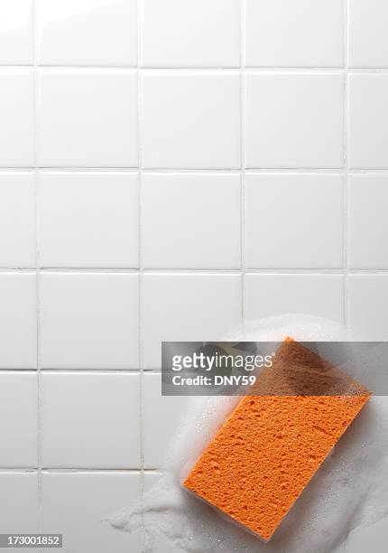 orange soapy sponge on white bathroom tiles - brillos stockfoto's en -beelden