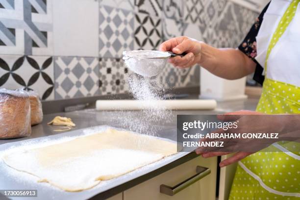 woman sprinkling flour on batter in a bakery kitchen - sifting stock pictures, royalty-free photos & images