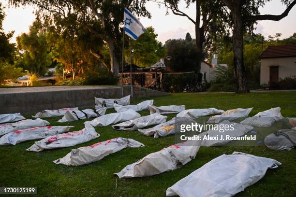 An Israeli flag flies over body bags of over 20 dead Hamas militants with the word "terrorist" written in Hebrew, on a main field at Kibbutz Be'eri,...