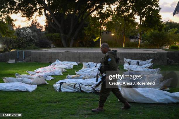 An IDF soldier walks past body bags of over 20 dead Hamas militants with the word "terrorist" written in Hebrew, on a main field at Kibbutz Be'eri,...