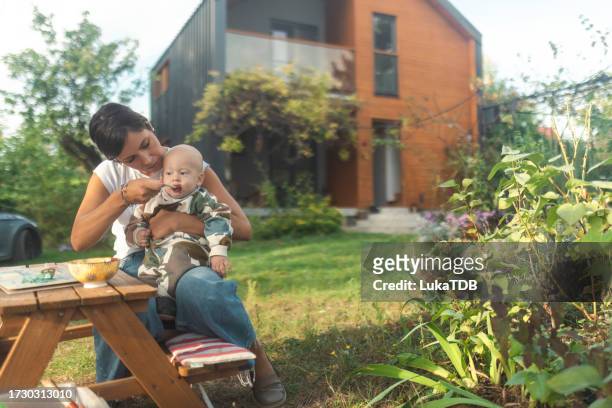 nanny feeds the baby boy in the yard with children's porridge - child eating cereal stock pictures, royalty-free photos & images