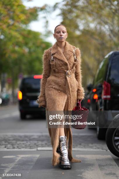 Guest wears a brown fluffy faux fur trench coat, silver moon boots, a red large bag, outside Rabanne, during the Womenswear Spring/Summer 2024 as...