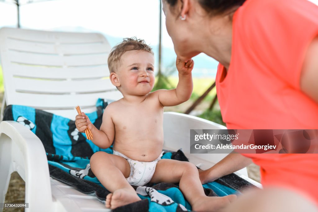 Baby Boy Trying To Aim Mother's Mouth While Play Feeding Her At The Beach