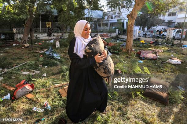Woman reacts while holding a pillow as she stands amidst debris outside the site of the Ahli Arab hospital in Gaza City on October 18, 2023 in the...