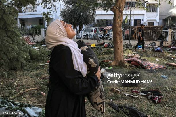 Woman reacts while holding a pillow as she stands amidst debris outside the site of the Ahli Arab hospital in Gaza City on October 18, 2023 in the...