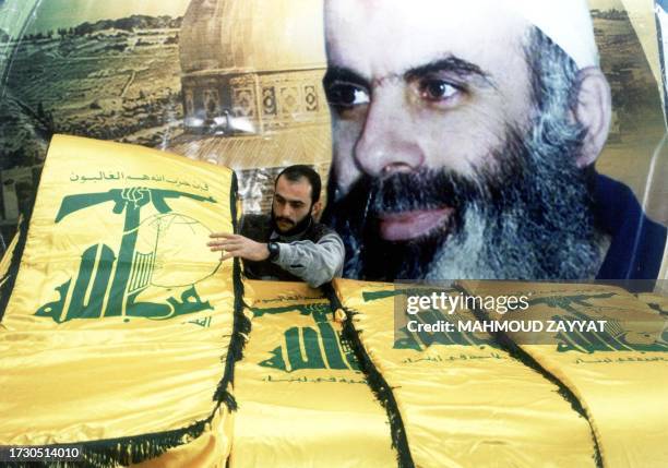 Hezbollah member places yellow flags of the guerrilla group in front of a huge portrait of Sheikh Abdel Karim Obeid in the southern Lebanese town of...