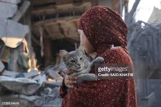 Palestinian girl carries a cat as she inspects the damage following Israeli bombardment in Rafah in the southern Gaza Strip, on October 18 amid...