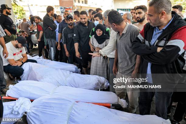 Graphic content / People gather by the wrapped bodies of victims who died in an overnight strike at the Ahli Arab hospital in Gaza City on October...